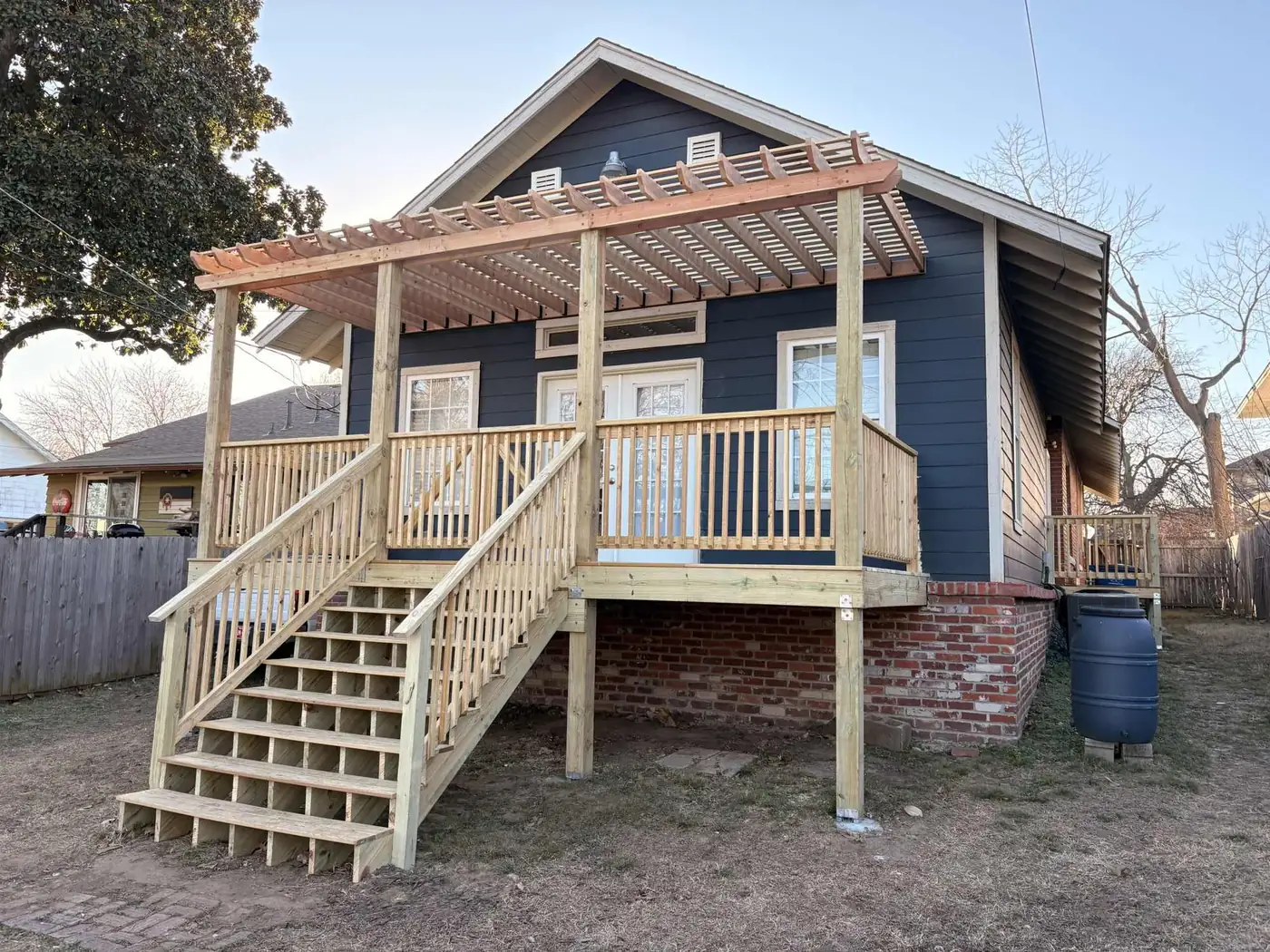 Elevated pressure-treated deck with stairs and a pergola on the back of a blue house