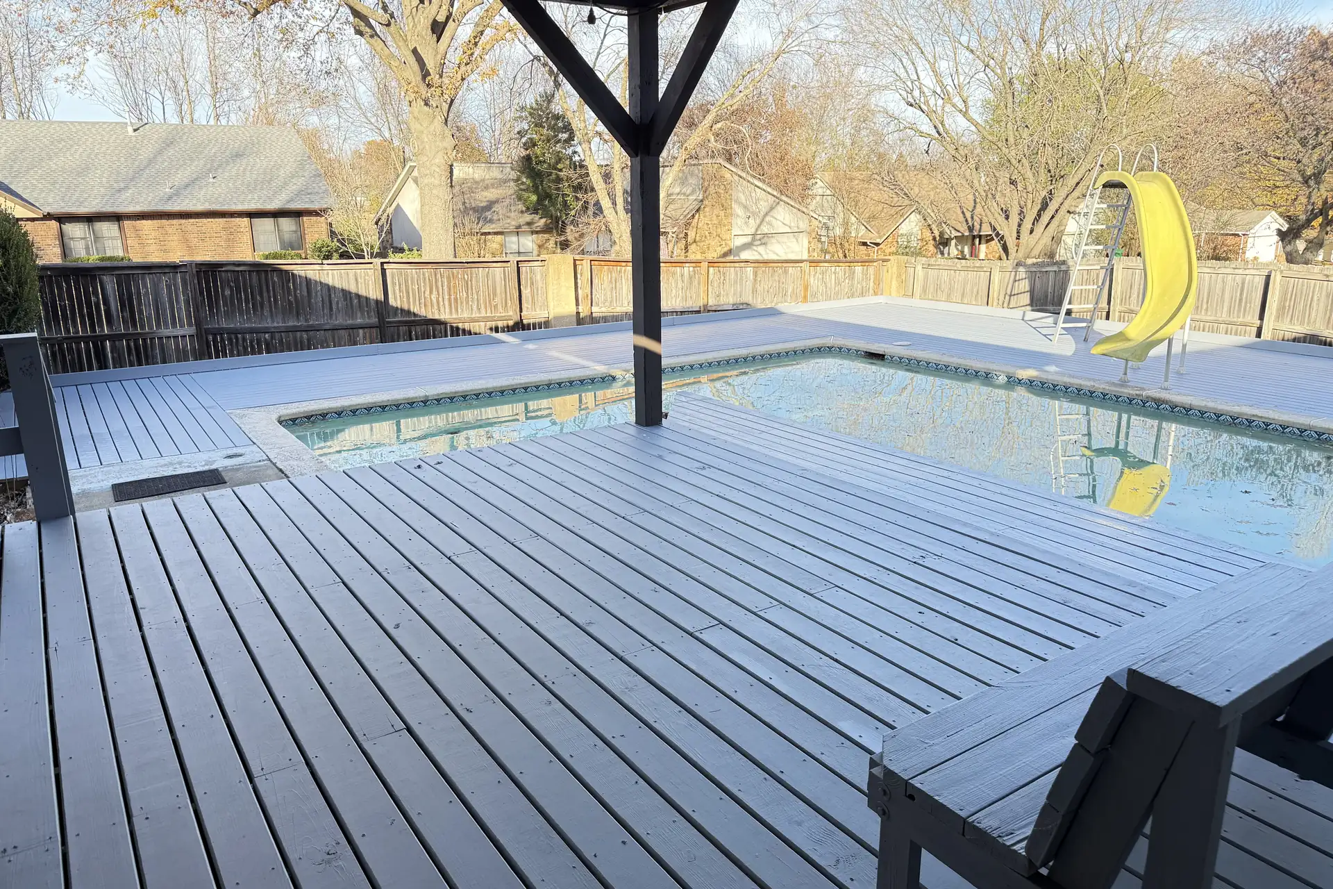 Gray composite deck under a roofed pavilion wrapping a backyard pool