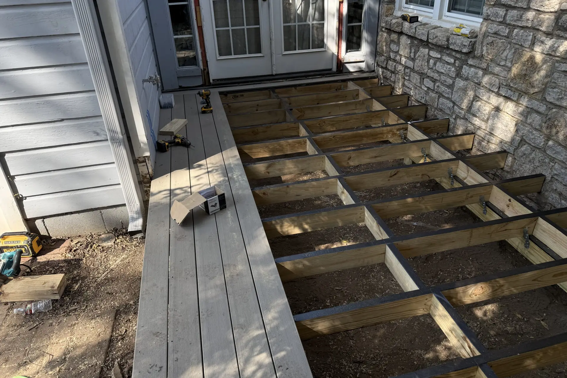 Deck framing in progress with new joists set against a stone home