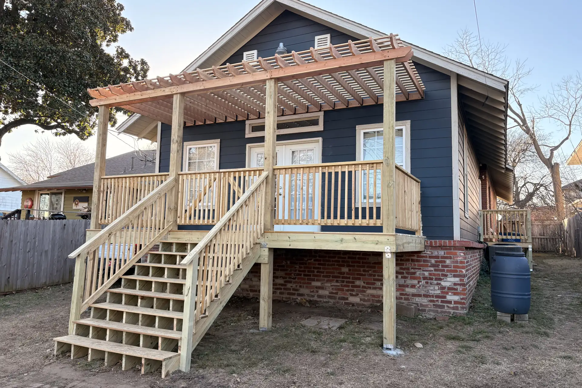 Elevated wood deck with pergola and stairs on a blue bungalow