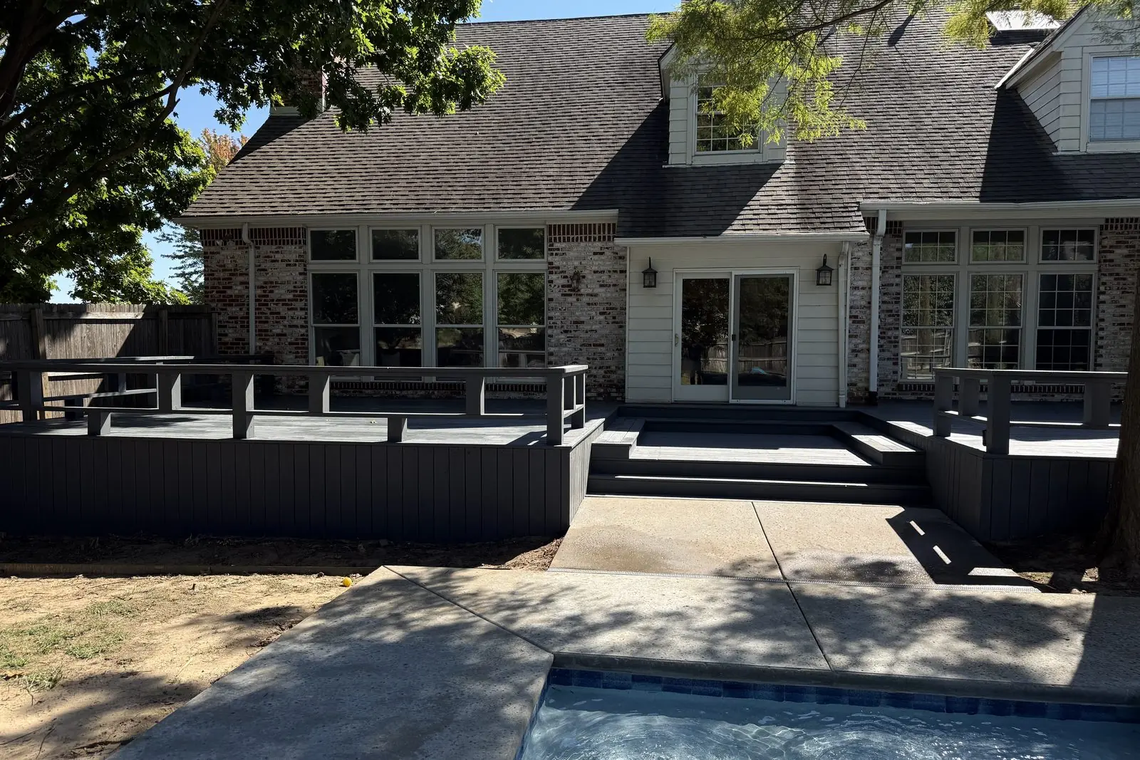 Dark composite deck with bench railing and stairs down to a backyard pool