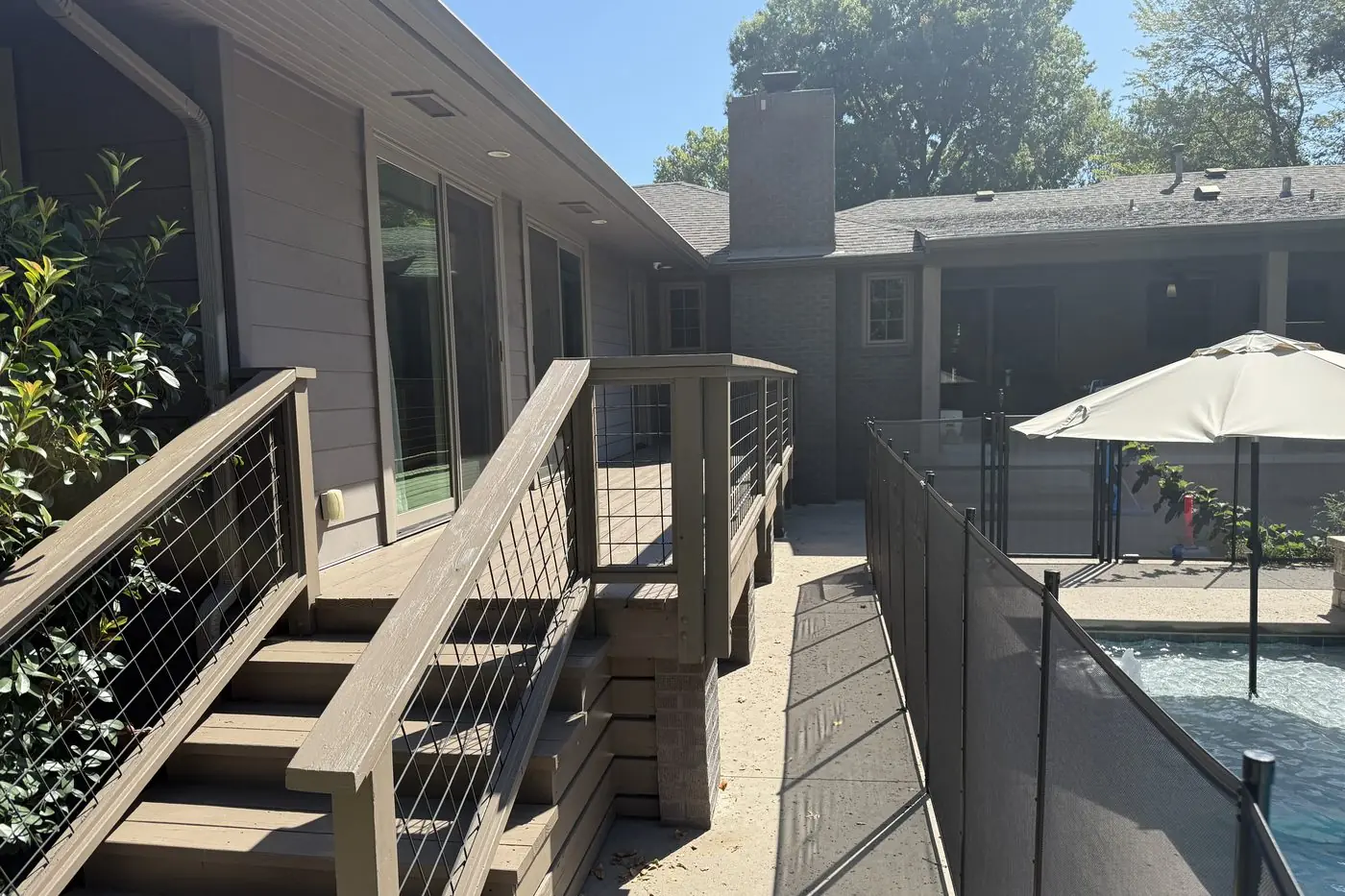 Composite deck stairs with hog-wire railing panels leading down to a pool patio