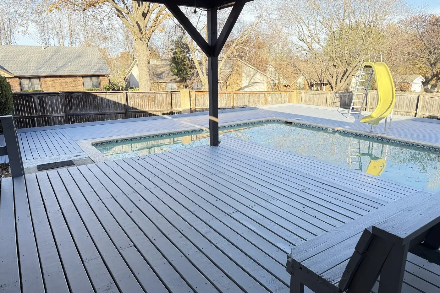 Gray-painted wood deck under a gazebo roof wrapping a backyard pool