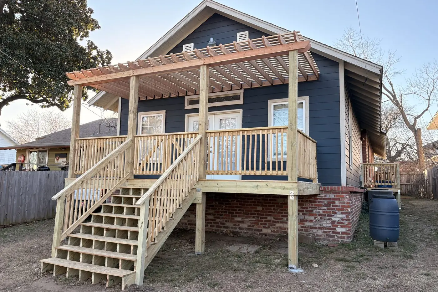 Two-story pressure-treated deck with pergola, railing, and full stair run on a blue bungalow